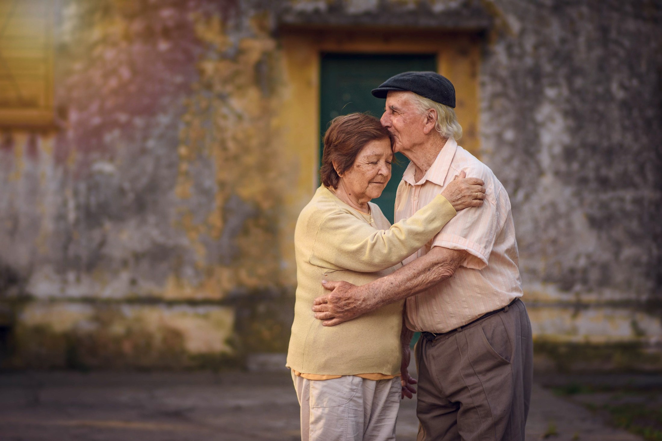 Couple âgé enlacé devant une maison